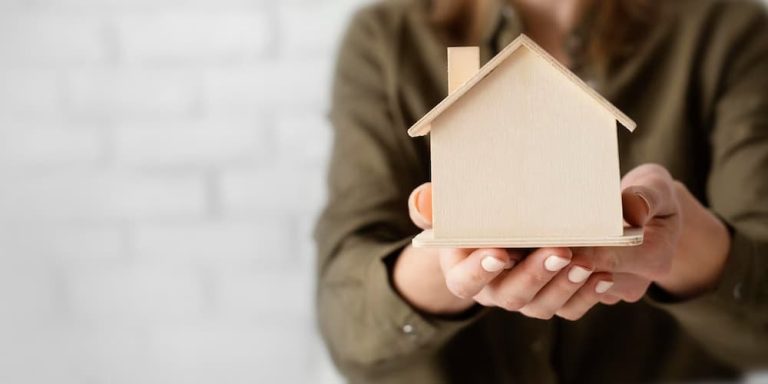 Mujer sosteniendo figura de casa hecha en madera