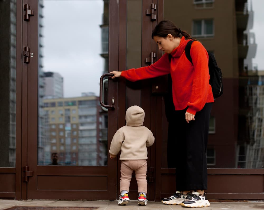 Mujer con niño pequeño frente a puerta cerrada de edificio urbano