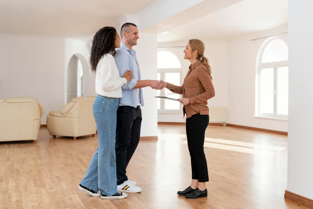 Pareja saludando a agente inmobiliaria en piso luminoso