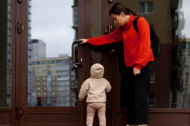Mujer con niño pequeño frente a puerta cerrada de edificio urbano