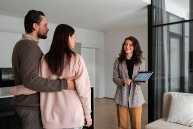 Pareja visitando piso con agente inmobiliaria mostrando plano en tablet