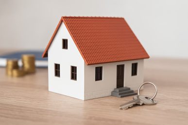Maqueta de casa blanca con tejado rojo junto a llaves sobre una mesa